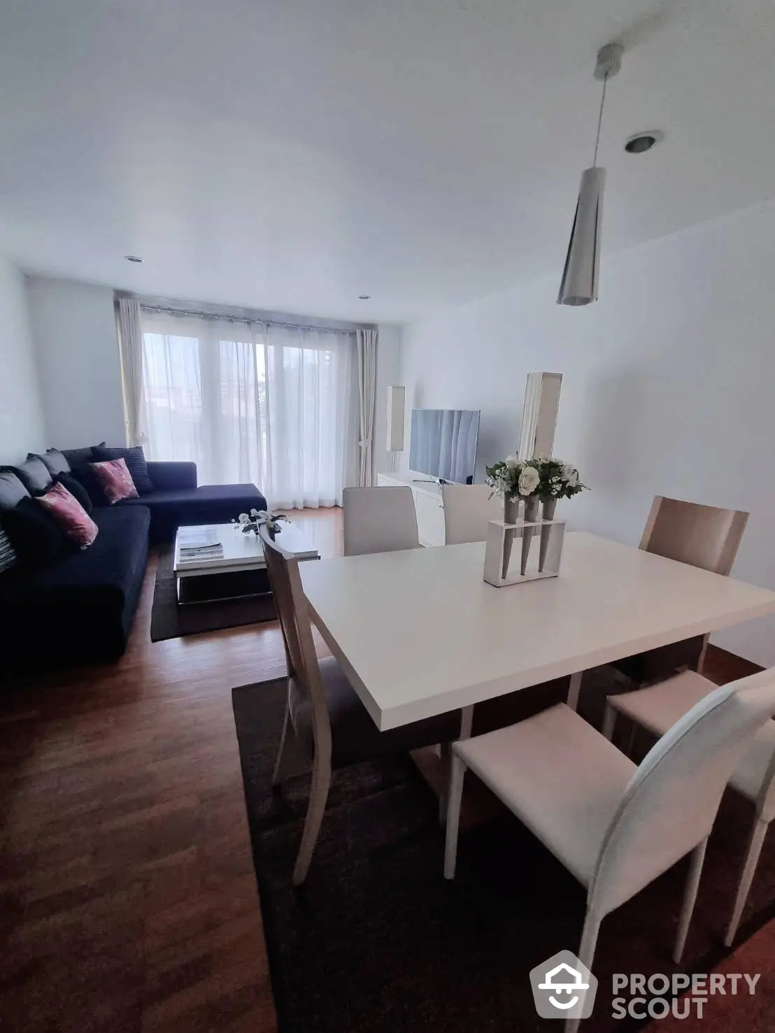 Spacious and modern living room with elegant dining set, cozy sofa, and ample natural light filtering through sheer curtains, perfect for comfortable urban living.