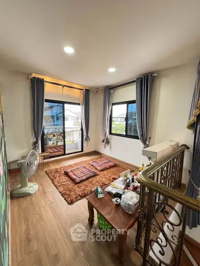 Cozy living room with large windows and wooden flooring, featuring a small table and cushions for seating.
