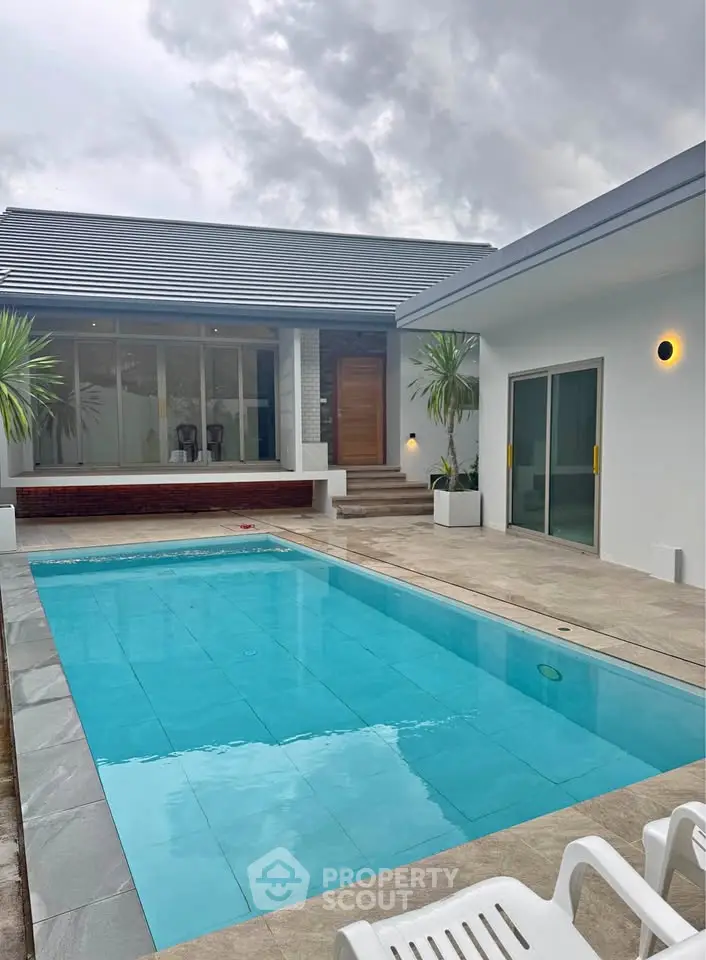 Modern villa with sleek pool and stylish architecture under cloudy sky.