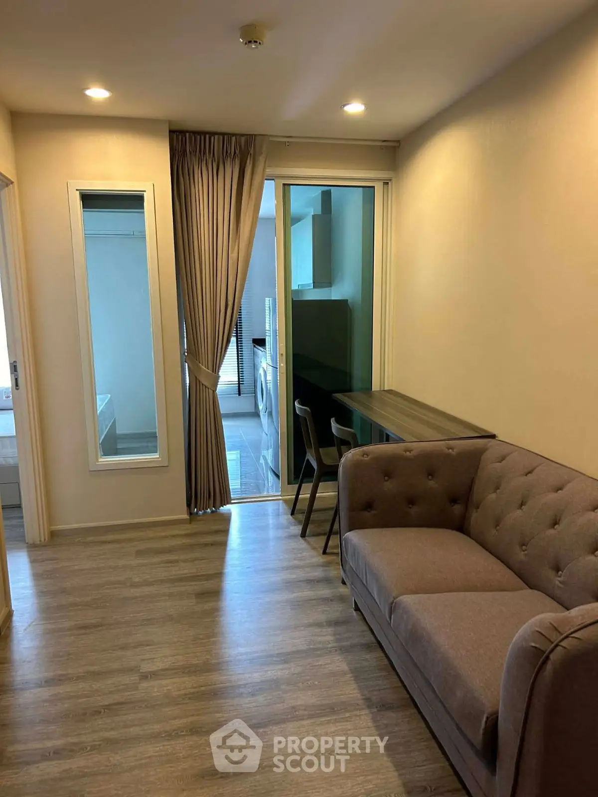 Cozy living room with modern sofa and dining area, leading to a kitchen with washing machine.