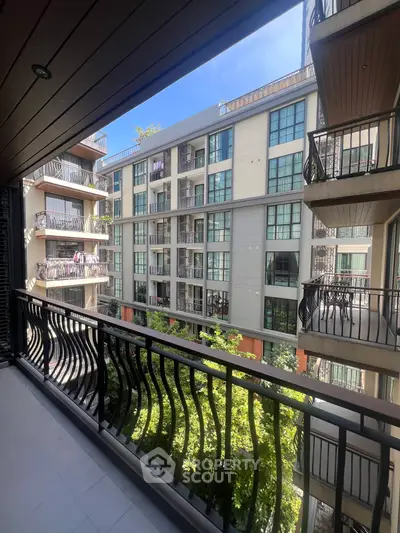 Spacious balcony with elegant railing overlooking modern apartment complex and lush greenery.
