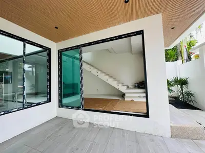 Modern home with large windows and sleek staircase, featuring a stylish wooden ceiling and spacious patio area.