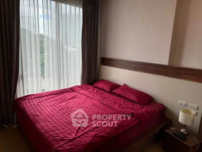 Cozy bedroom with red bedding and large window offering natural light