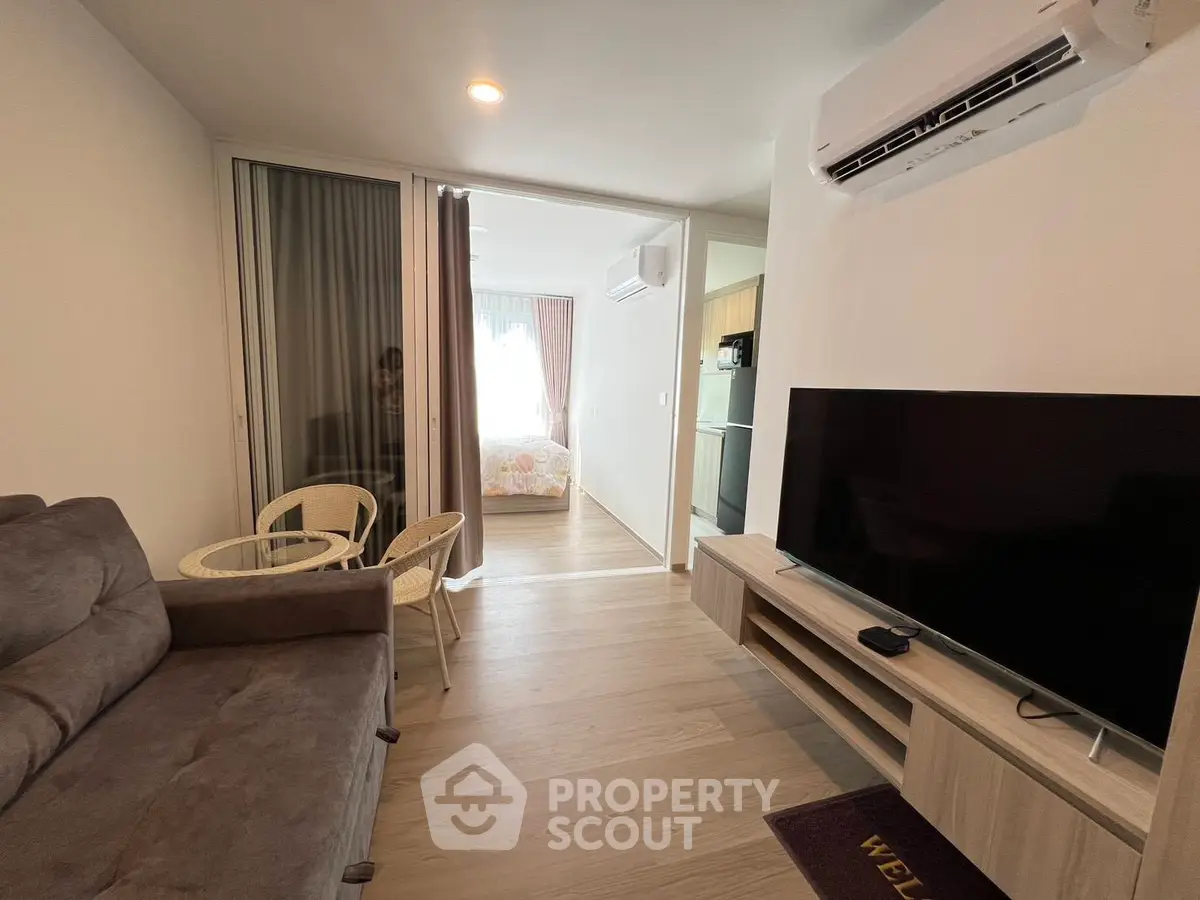 Modern living room with cozy sofa, TV, and open view to bedroom