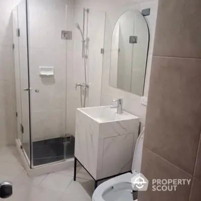 Modern bathroom with sleek glass shower enclosure, stylish square basin, and large mirror, all complemented by neutral tilework.