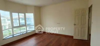Spacious empty room with wooden flooring and large windows offering natural light and neighborhood view.