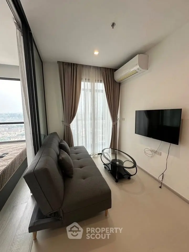 Modern living room with sleek sofa, glass coffee table, and wall-mounted TV, featuring large window with city view.