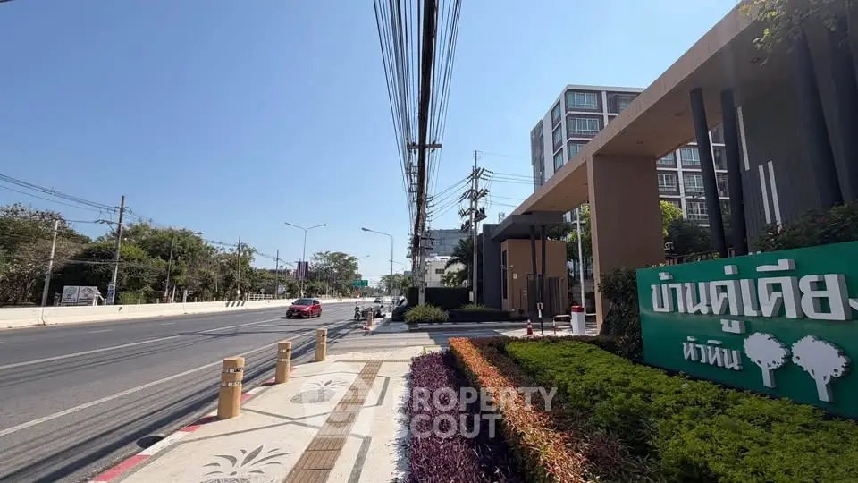 Modern residential building entrance with lush landscaping and street view.
