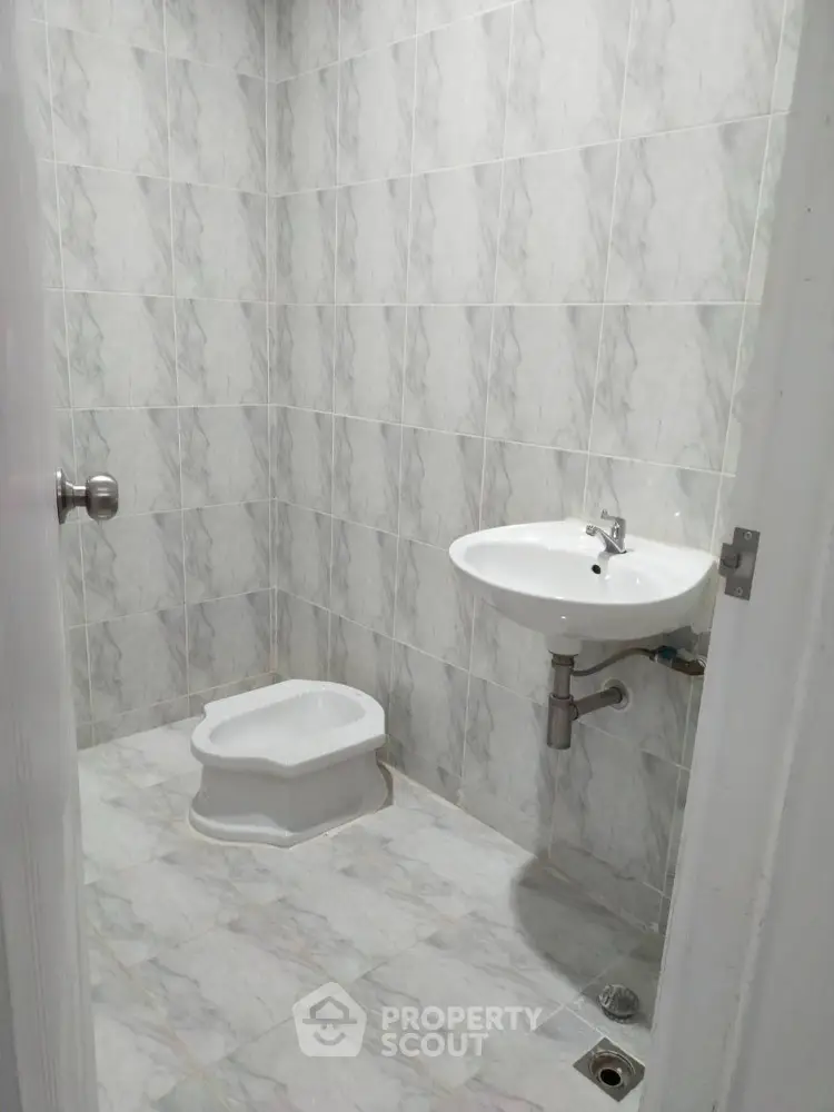 Minimalist bathroom with tiled walls and floor featuring a wall-mounted sink and squat toilet.