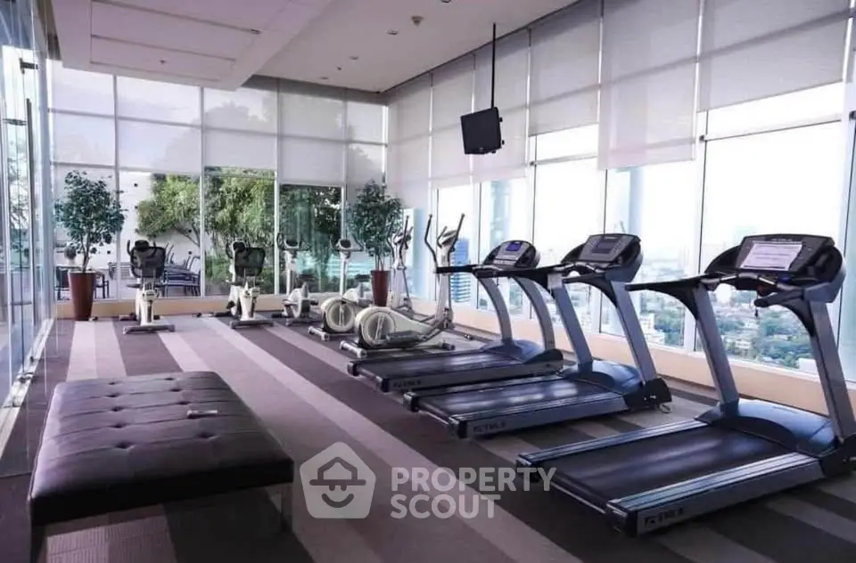 Spacious gym with modern equipment and panoramic city views in luxury residential building.