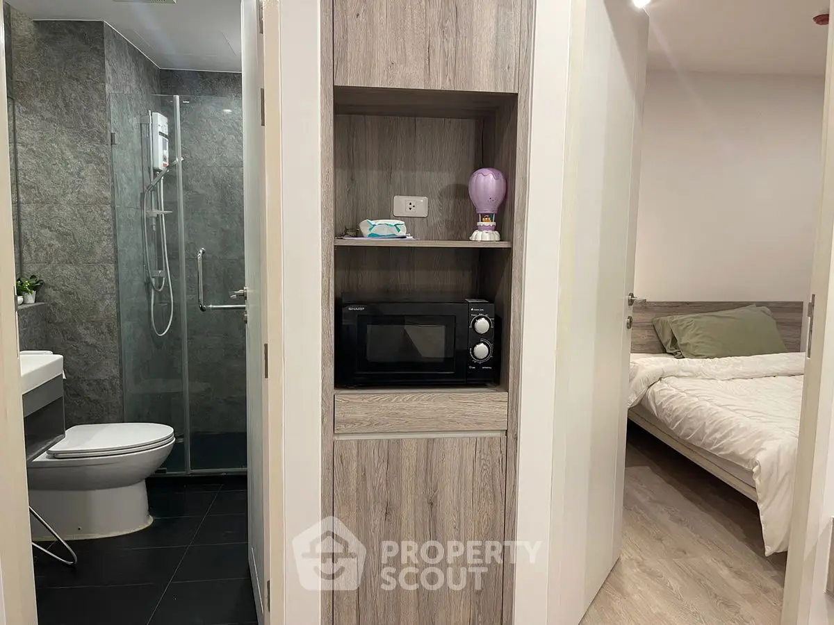 Modern apartment interior with bathroom and bedroom view, featuring sleek design and compact microwave setup.