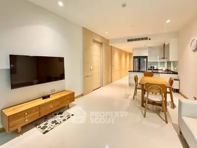 Spacious modern living room with open kitchen and dining area, featuring sleek furniture and bright lighting.