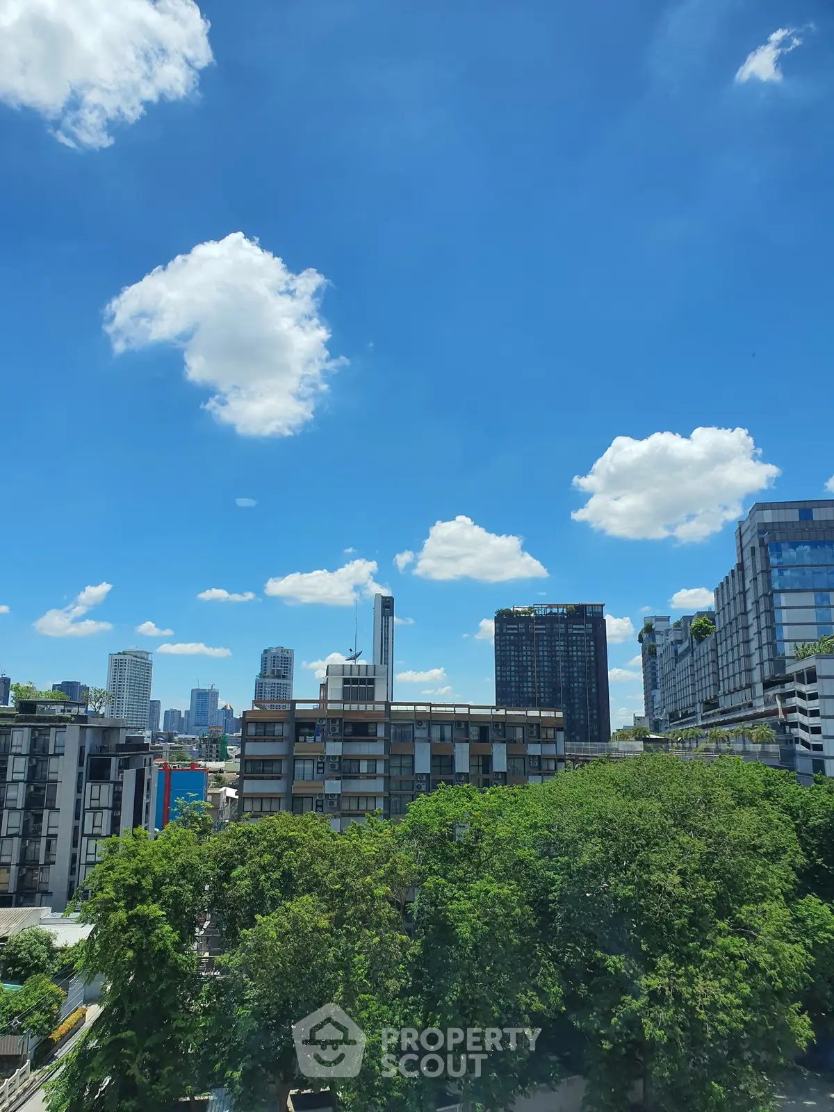 Stunning cityscape view with modern buildings and lush greenery under a bright blue sky.