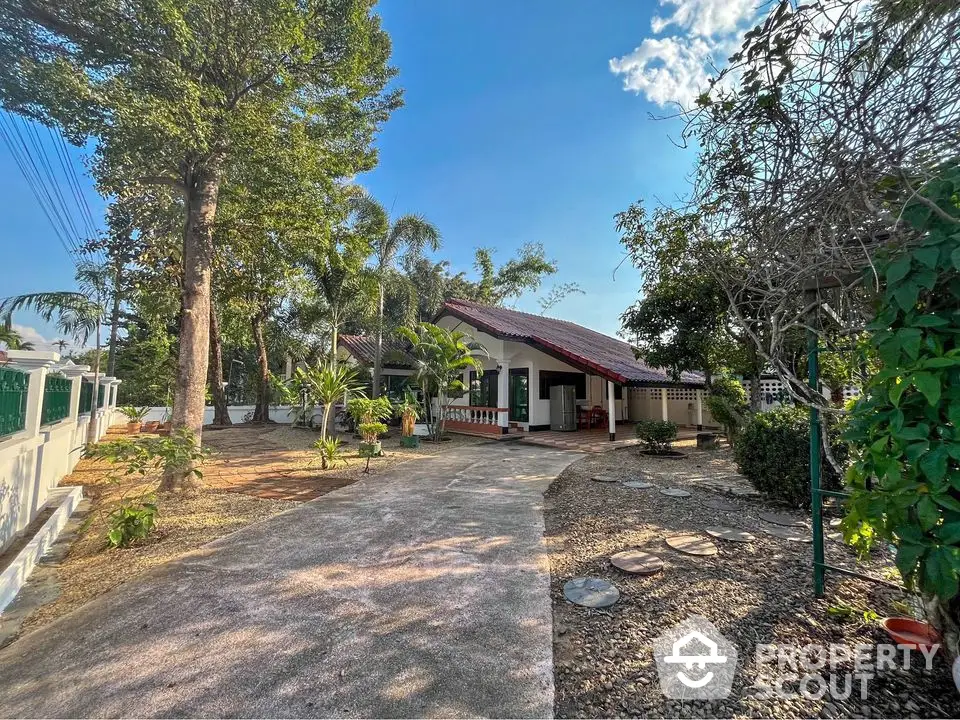 Charming single-story house with spacious garden and driveway, surrounded by lush greenery.