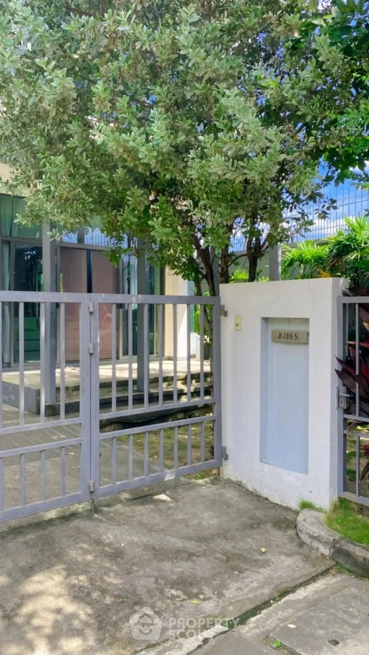 Charming residential entrance with lush greenery and secure gate in a serene neighborhood.