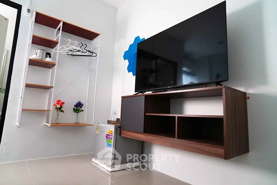 Modern living room with wall-mounted TV, sleek shelves, and compact fridge in a stylish apartment.