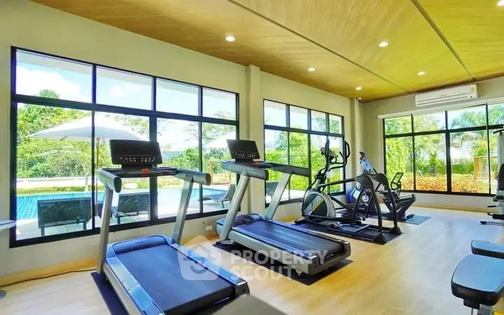 Modern gym with large windows overlooking a pool and garden, featuring state-of-the-art exercise equipment.