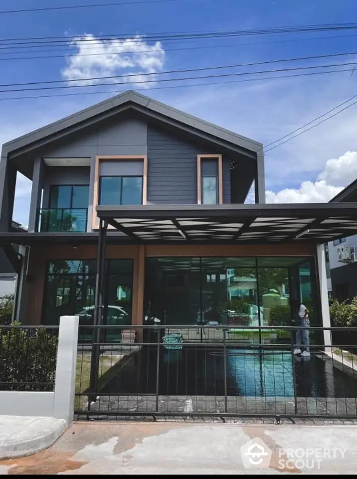 Modern two-story home with expansive glass facade and sleek design, featuring a private pool and covered parking, set under a clear blue sky.