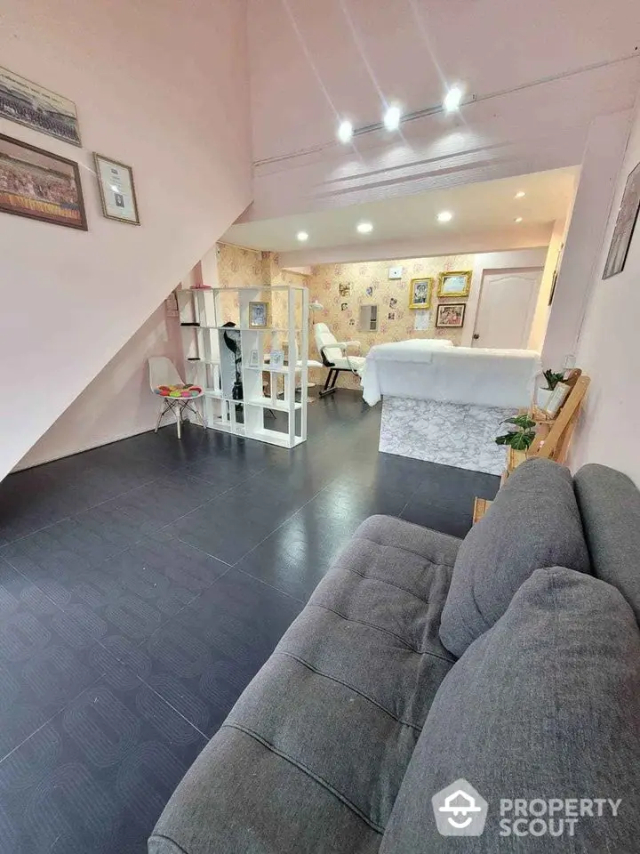 Charming attic bedroom with cozy living space, featuring sleek dark flooring, comfortable grey sofa, and ambient lighting, ideal for a modern urban retreat.