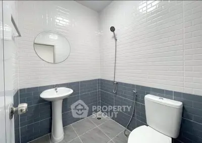 Modern bathroom with sleek tiles and minimalist fixtures, featuring a round mirror and a handheld shower.