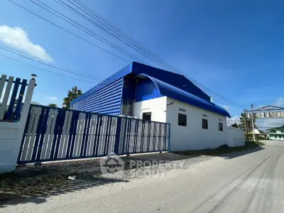 Industrial warehouse with blue roof and secure gated entrance on sunny day