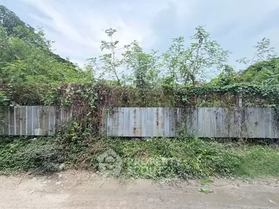 Vacant land with overgrown vegetation and metal fence, ideal for development opportunities.