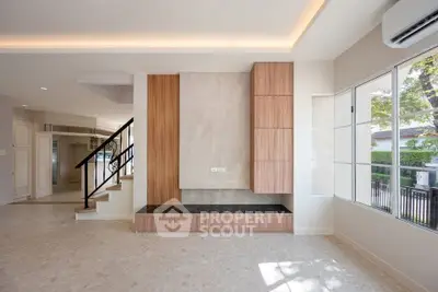 Modern living room with elegant staircase and large windows, featuring sleek wood paneling and natural light.