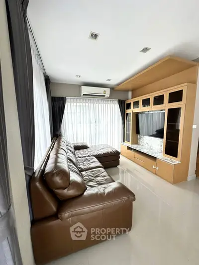 Spacious living room with leather sofa and large TV unit, perfect for relaxation.