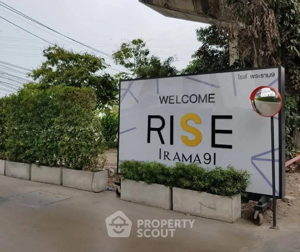 Welcome sign for Rise Rama 9, a modern real estate development with lush greenery.