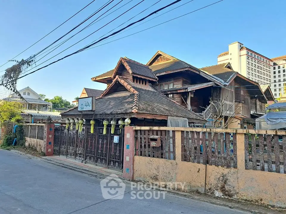 Charming traditional wooden house with intricate roof design and gated entrance.