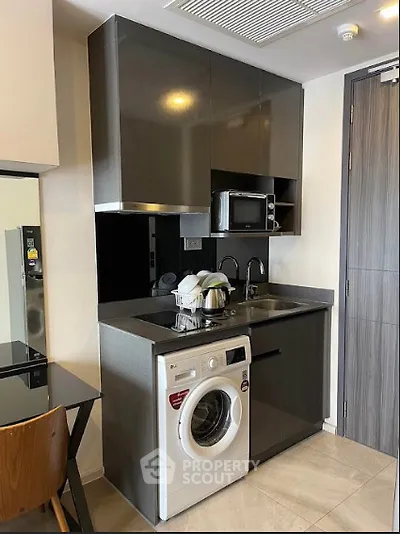 Modern compact kitchen with washing machine and microwave in sleek apartment.