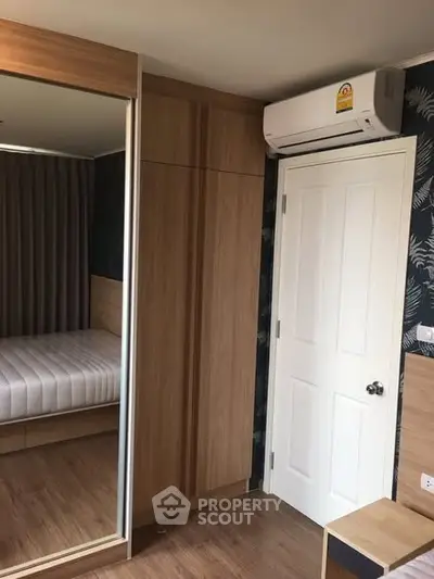 Modern bedroom with mirrored wardrobe and air conditioning unit, featuring sleek wooden finishes.