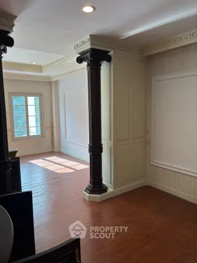 Elegant interior with classic columns and wooden flooring, featuring abundant natural light through large windows.