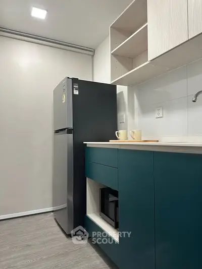 Modern kitchen with sleek fridge and teal cabinetry, perfect for urban living.