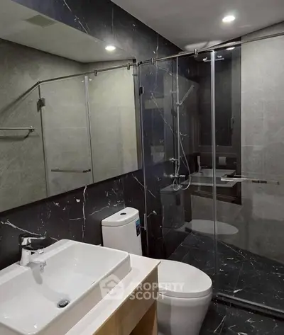 Modern bathroom with sleek black marble tiles and glass shower enclosure.