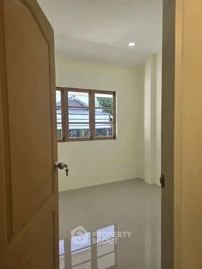 Bright and airy room with large window and glossy tiled floor, perfect for a cozy bedroom or home office.