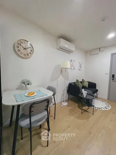 Cozy living room with modern decor and dining area, featuring wall clock and air conditioning.