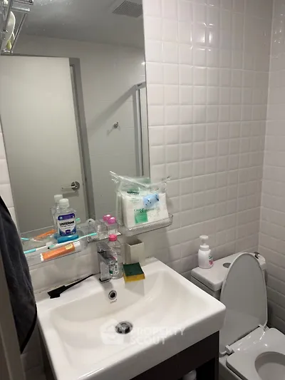 Compact bathroom with white tiles and modern fixtures, featuring a sink and toilet.