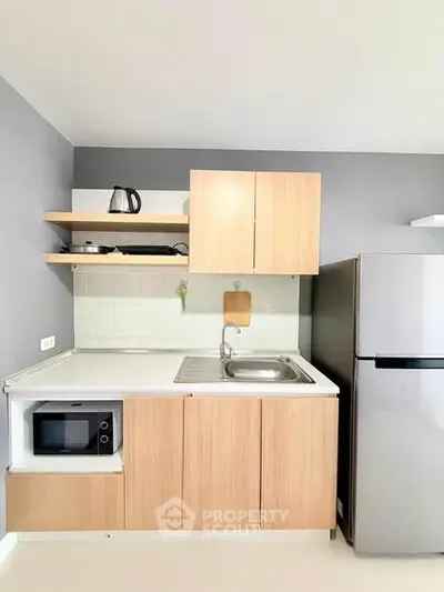 Modern compact kitchen with wooden cabinets, microwave, and stainless steel fridge in sleek apartment.