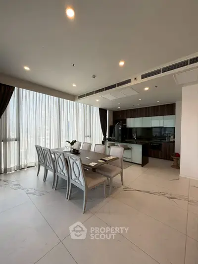 Spacious modern dining area with elegant table and open kitchen layout, featuring large windows and stylish decor.