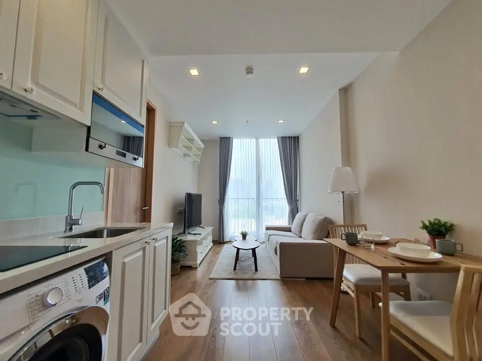 Modern living room with open kitchen, featuring sleek appliances and cozy seating area.