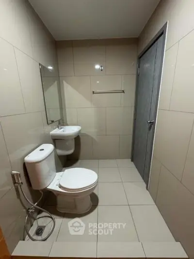 Modern bathroom with sleek fixtures and neutral tiles, featuring a toilet and wall-mounted sink.