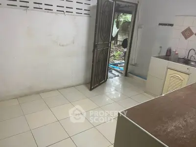 Simple kitchen with open door leading to backyard, tiled floor, and basic sink setup.