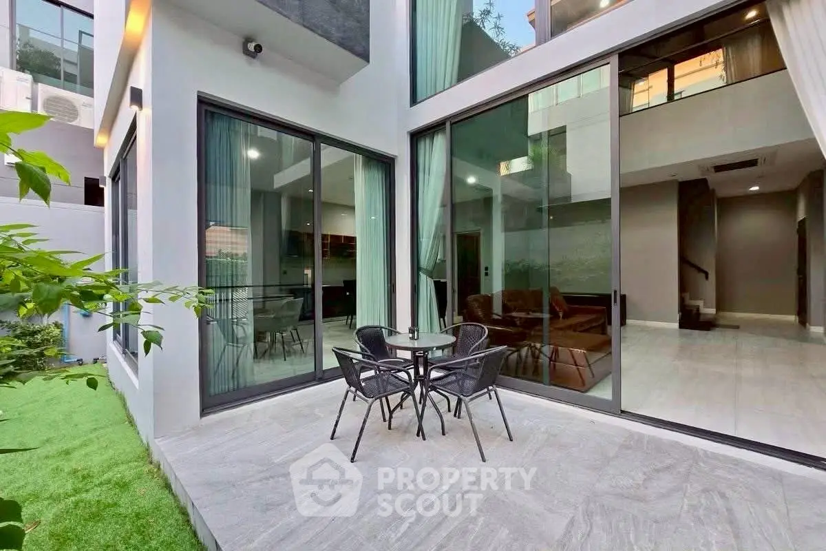 Modern home exterior with large glass doors and cozy patio seating area.