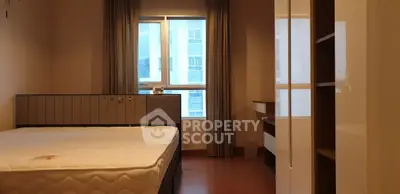 Spacious bedroom with large window and modern furnishings in urban apartment.