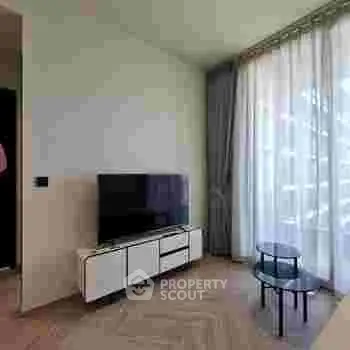 Modern living room with TV and stylish furniture, featuring large windows and natural light.