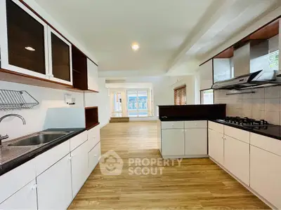 Spacious open-layout kitchen with modern gas stove and ample storage, leading to a bright living area with wooden flooring.