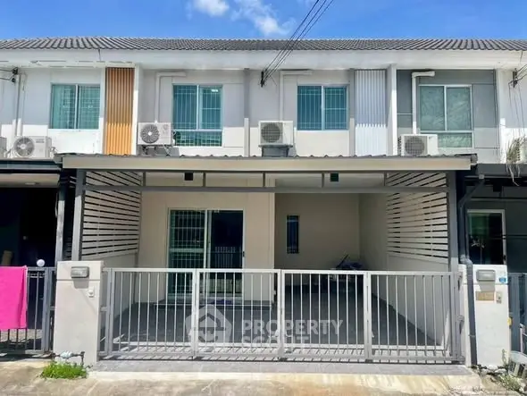 Modern townhouse exterior with gated parking and air conditioning units.