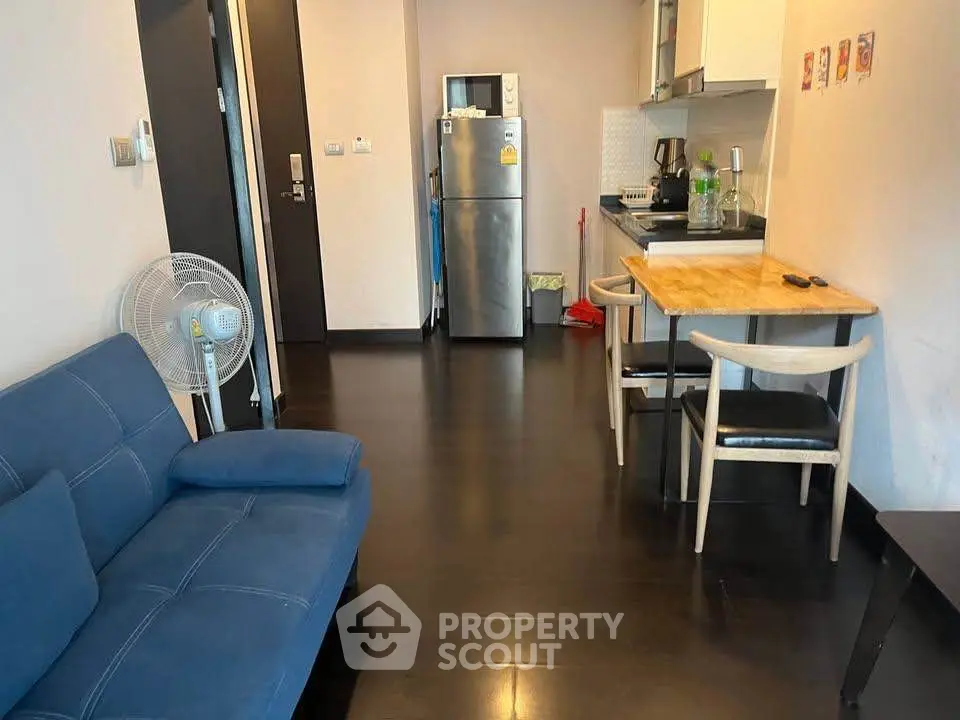 Modern apartment interior with sleek kitchen and cozy living area, featuring dark wood flooring and stylish furniture.