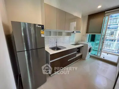 Modern kitchen with sleek cabinets, stainless steel fridge, and washing machine in a bright apartment.